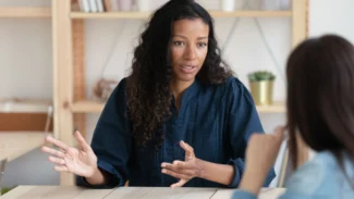 a woman sitting at a table talking to another woman.