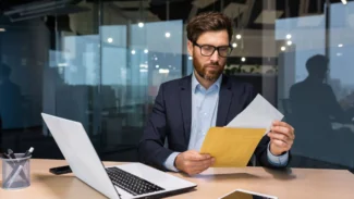 a man sitting at a desk holding opening an envelope