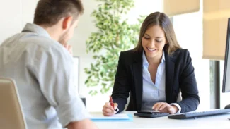 a woman using a calculator while sitting at a desk with a man in front of her