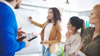 a group of people standing around a white board.