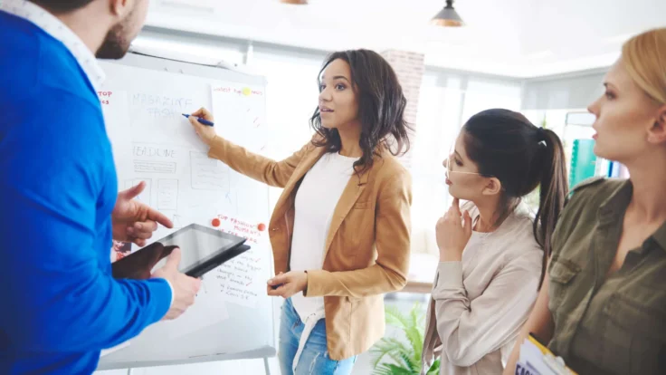 a group of people standing around a white board.