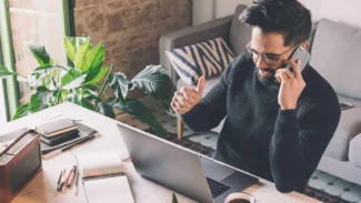 a man talking on a cell phone while using a laptop.