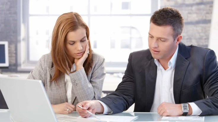 a man and woman sitting at a table looking at a laptop