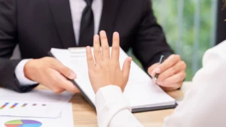 two people sitting at a table with papers and a pen.